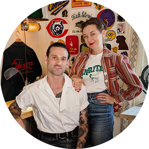 Two people posing together in a room with vintage decor and logos on the wall.
